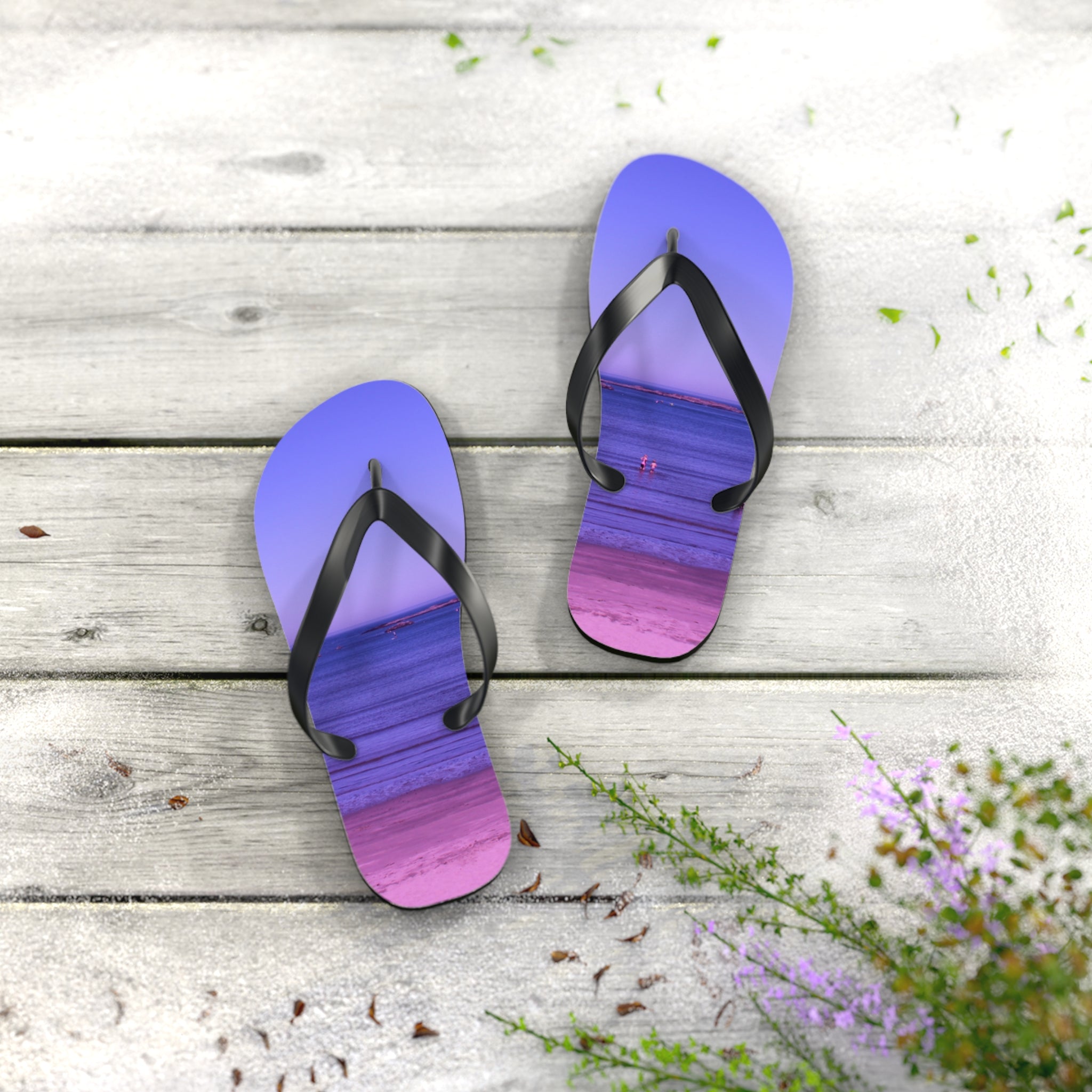 Purple and pink striped flip-flops on a wooden deck with scattered petals.