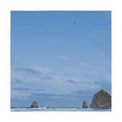 Sea stacks on a sandy beach with a red kite flying in the blue sky.