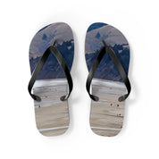Flip-flops with a scenic landscape of people on a beach and mountains.