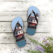 Blue flip-flops with a lighthouse print on weathered wood with greenery.