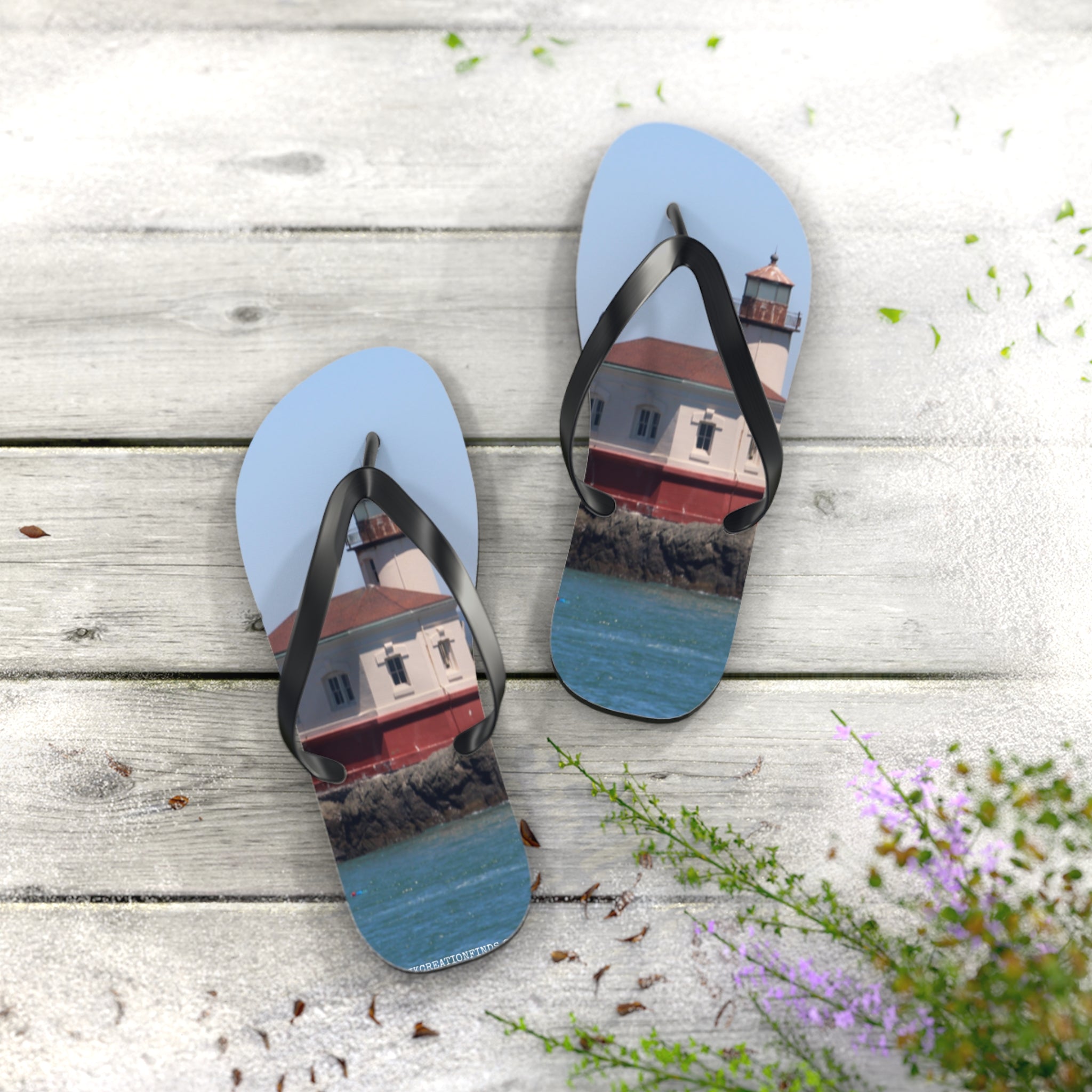 Blue flip-flops with a lighthouse print on weathered wood with greenery.