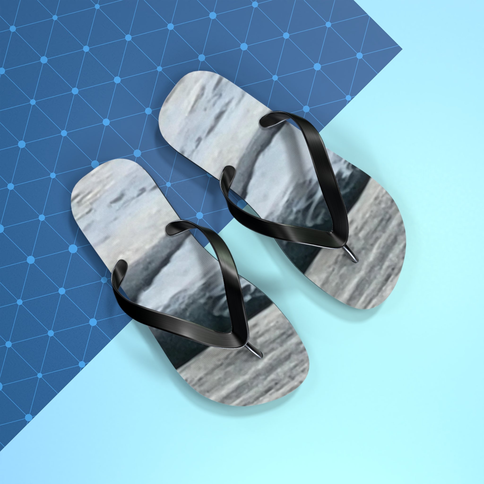 Black flip-flops with marble print on a light blue and patterned background.