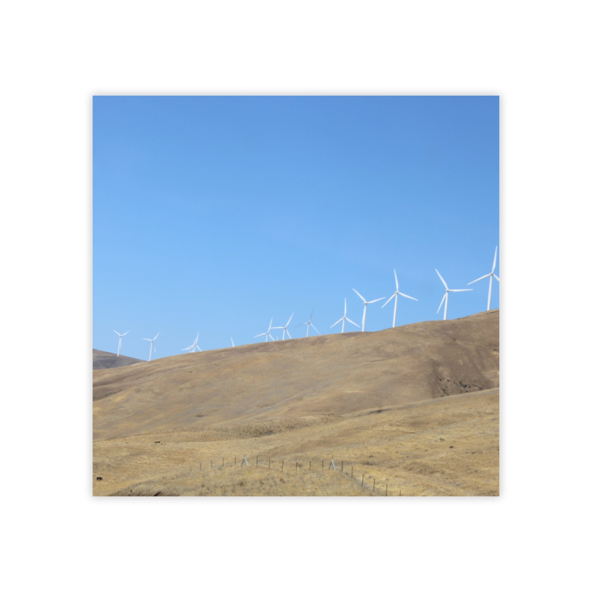 Wind turbines on a rolling, dry hillside under a clear blue sky.