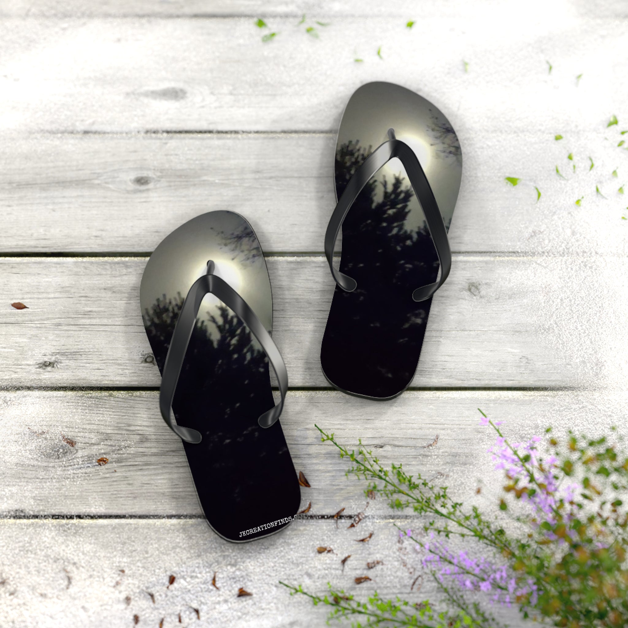 Black flip-flops with a sunset forest scene design on a wooden surface.