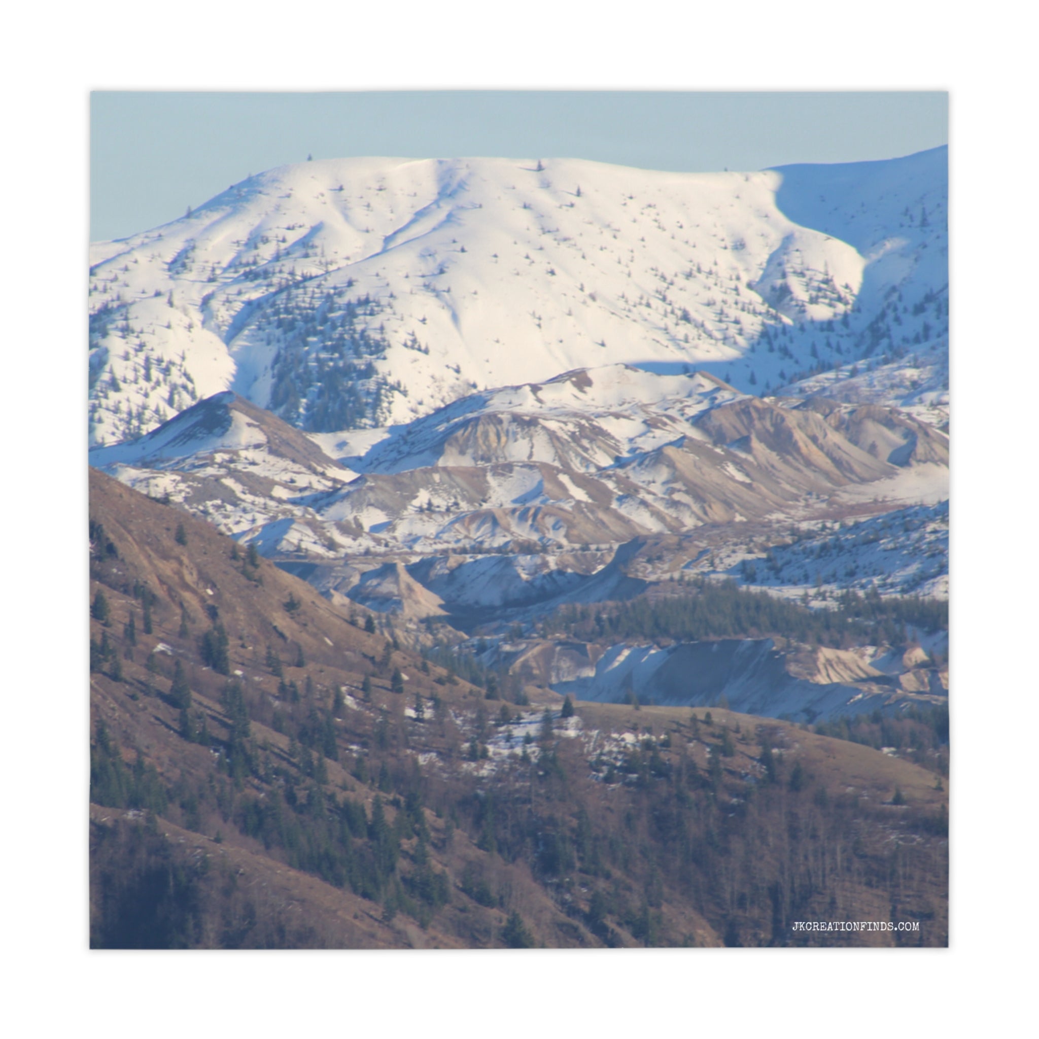 Snow-capped mountains and layered, treed hillsides under a bright sky.