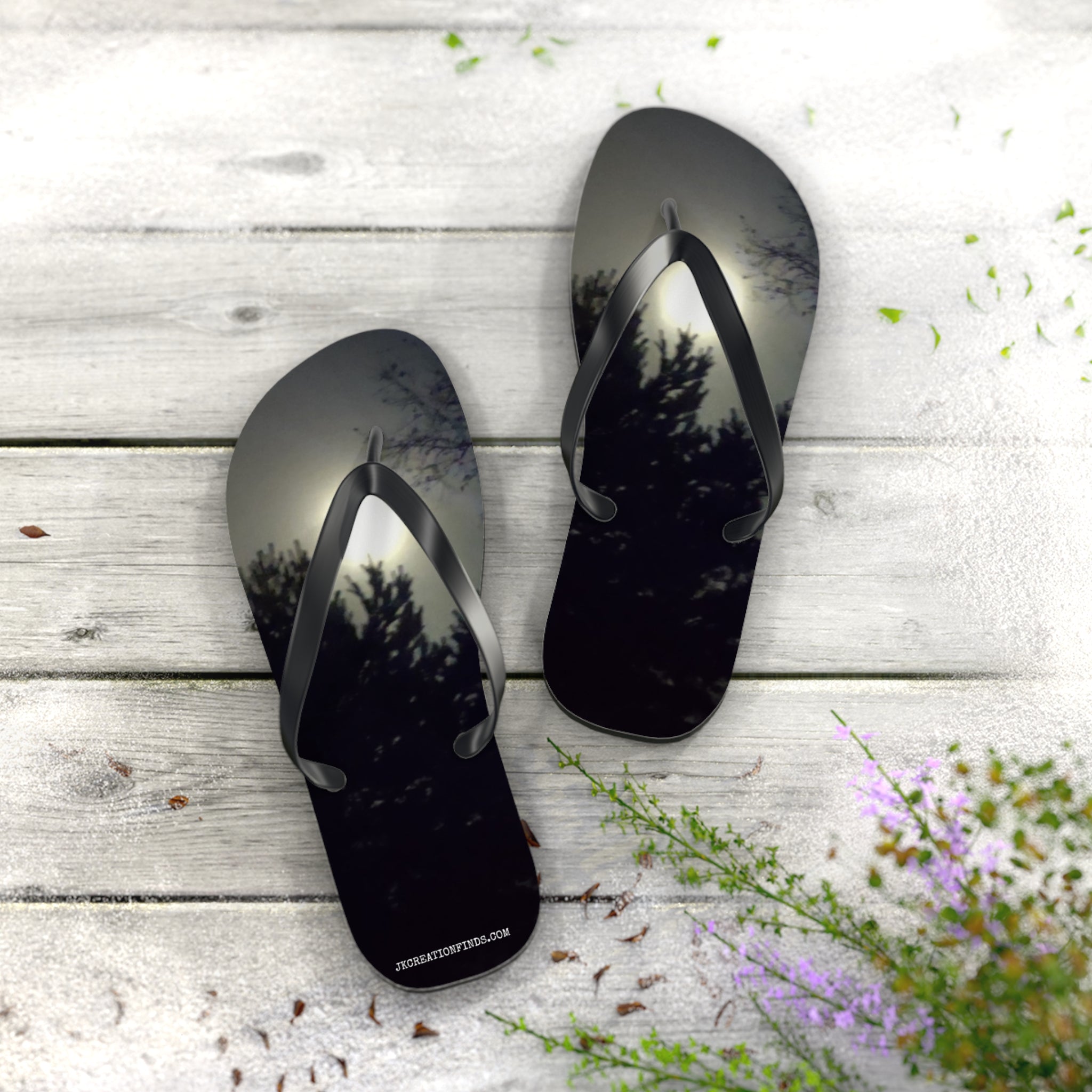 Black flip-flops with tree reflections on a weathered wooden surface.