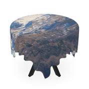Round tablecloth with a snowy mountain landscape print on a black table.