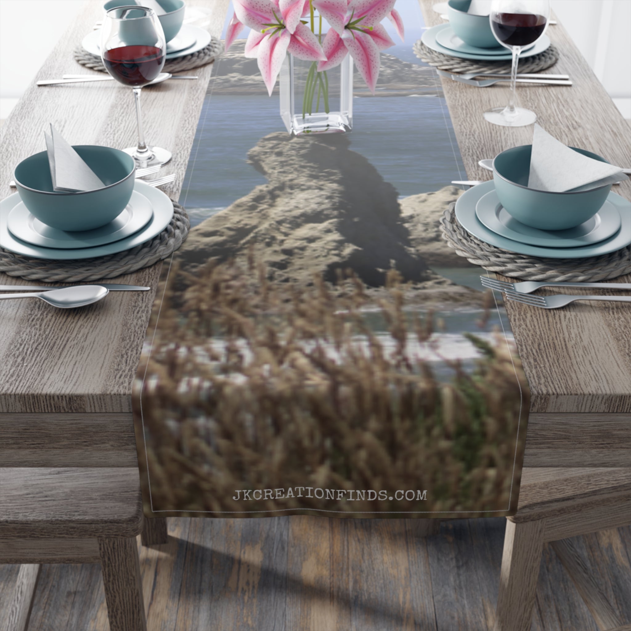 Table runner with rocky beach and ocean landscape, with flowers and place settings.