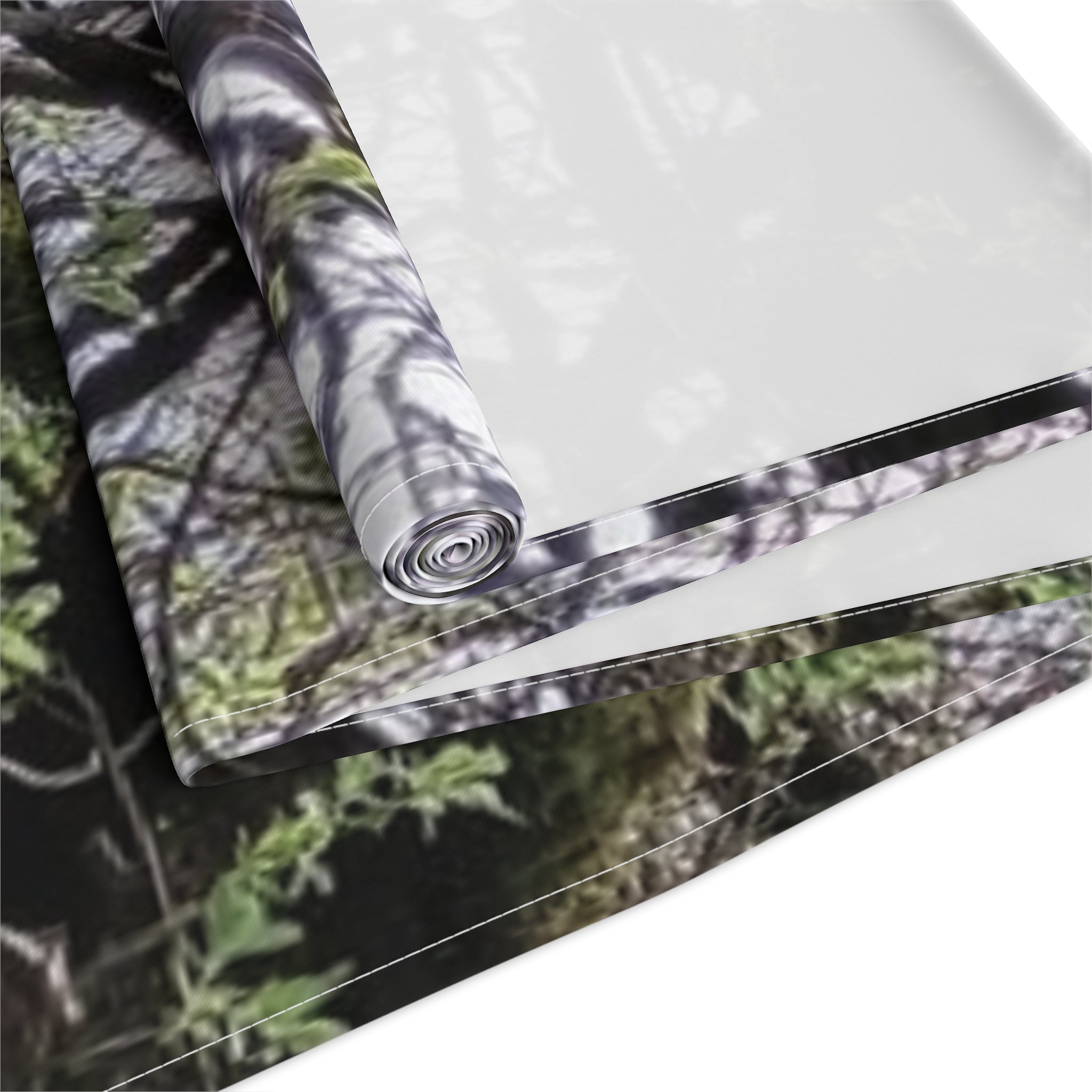 Rolled fabric with blurred forest camouflage pattern on white background.