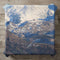 Textured pillow with snowy mountain landscape and pine trees.