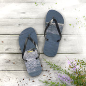 Flip-flops with ocean waves and surfers on wooden deck.
