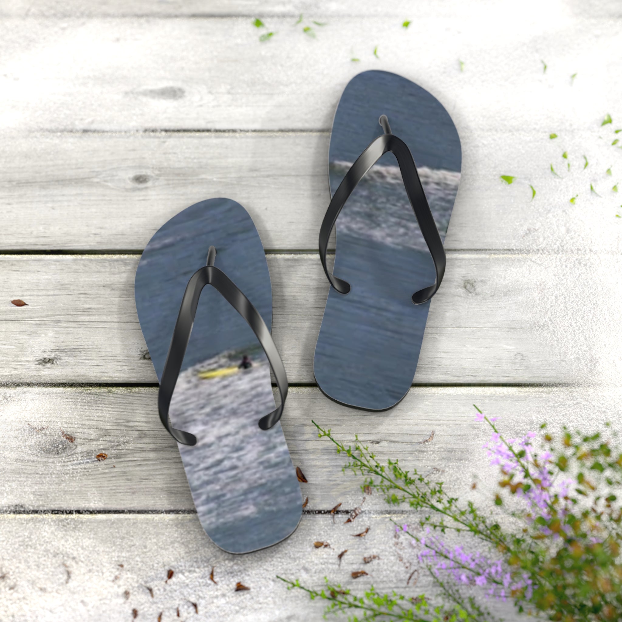 Flip-flops with ocean waves and surfers on wooden deck.