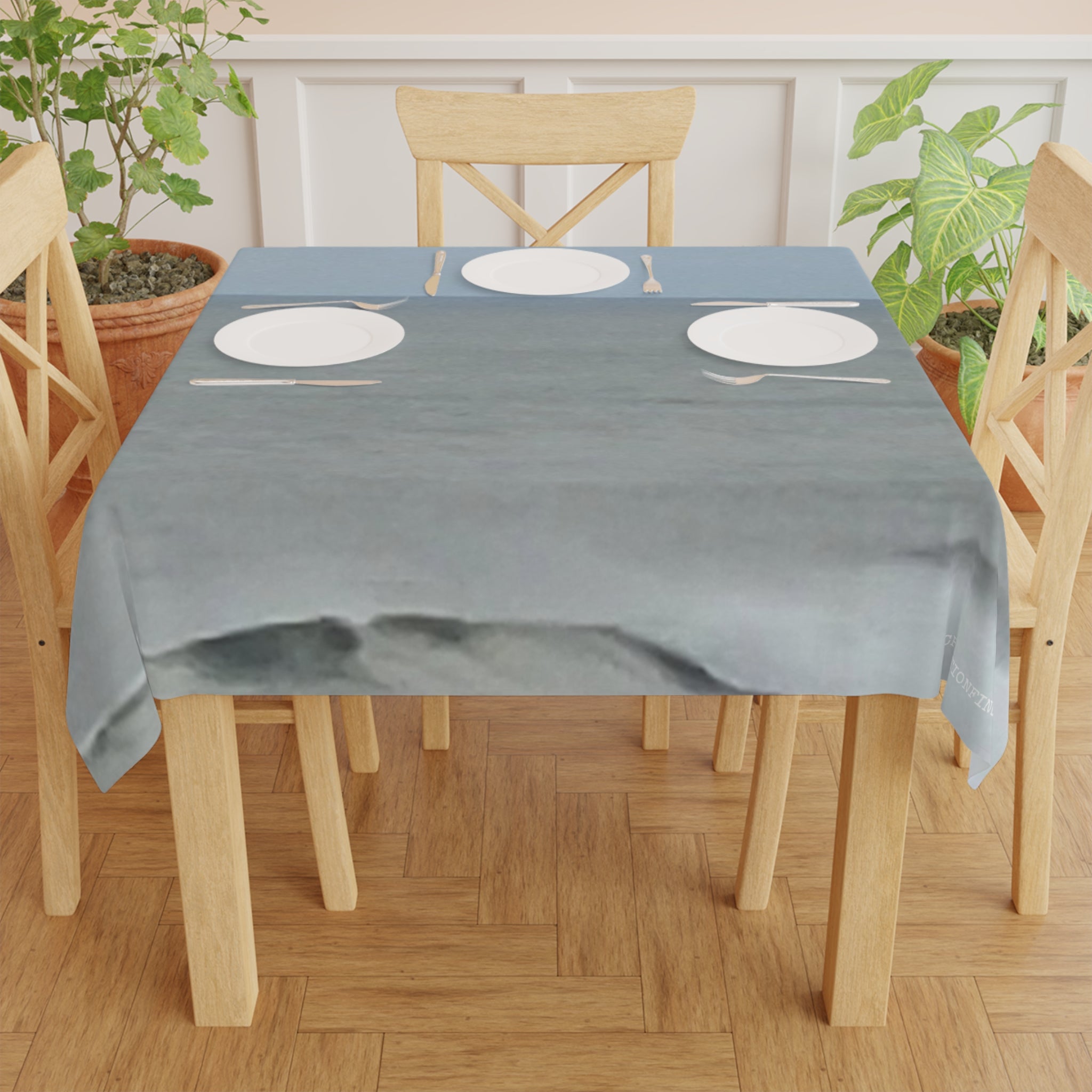 Tablecloth with place settings on wooden dining table with potted plants.