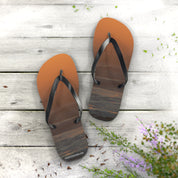 Flip-flops with a sunset ocean scene on the soles, on a wooden deck.