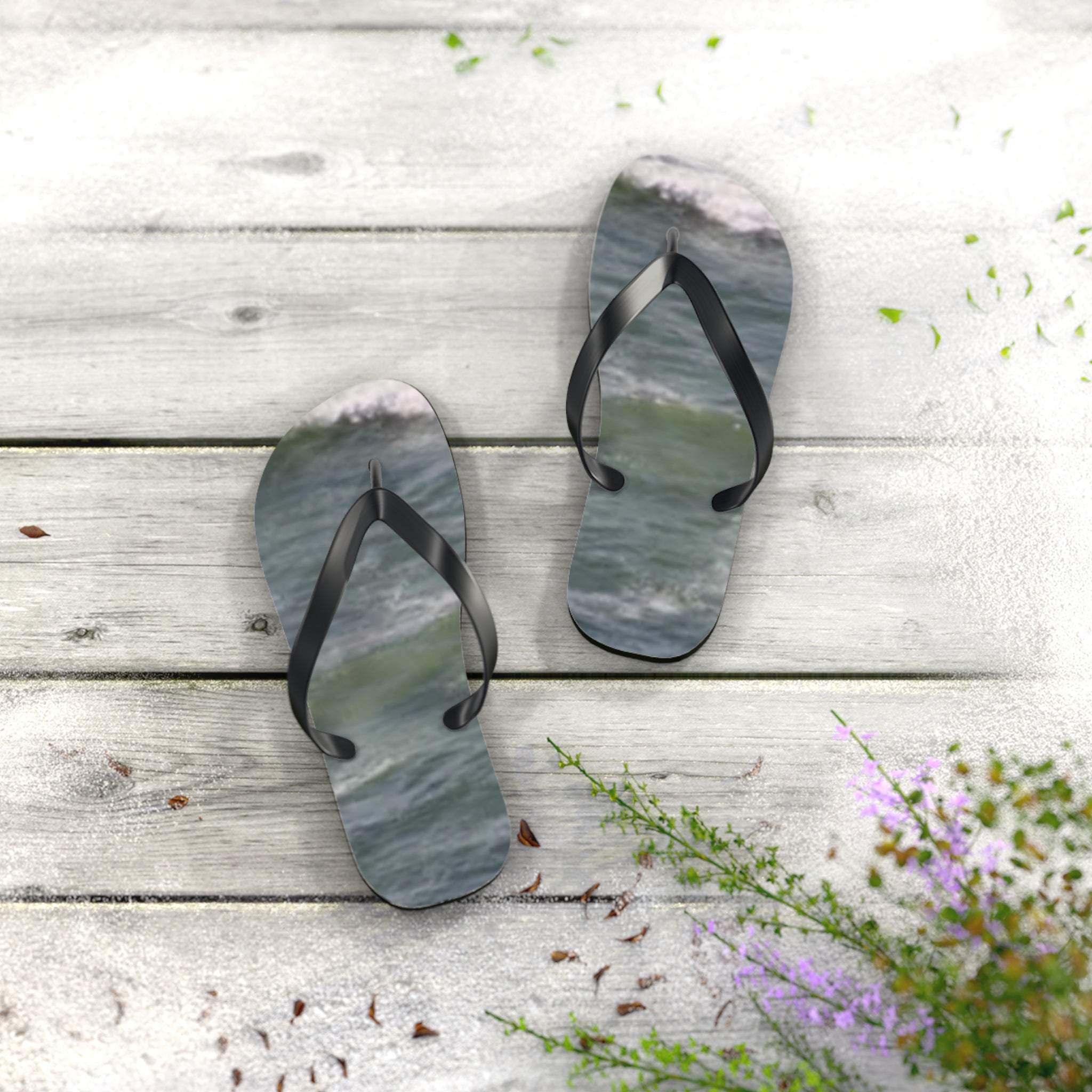 Ocean wave pattern flip-flops on a light wood surface with scattered green leaves.