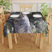 Tablecloth with a raccoon print, set with plates and silverware on a wooden table.