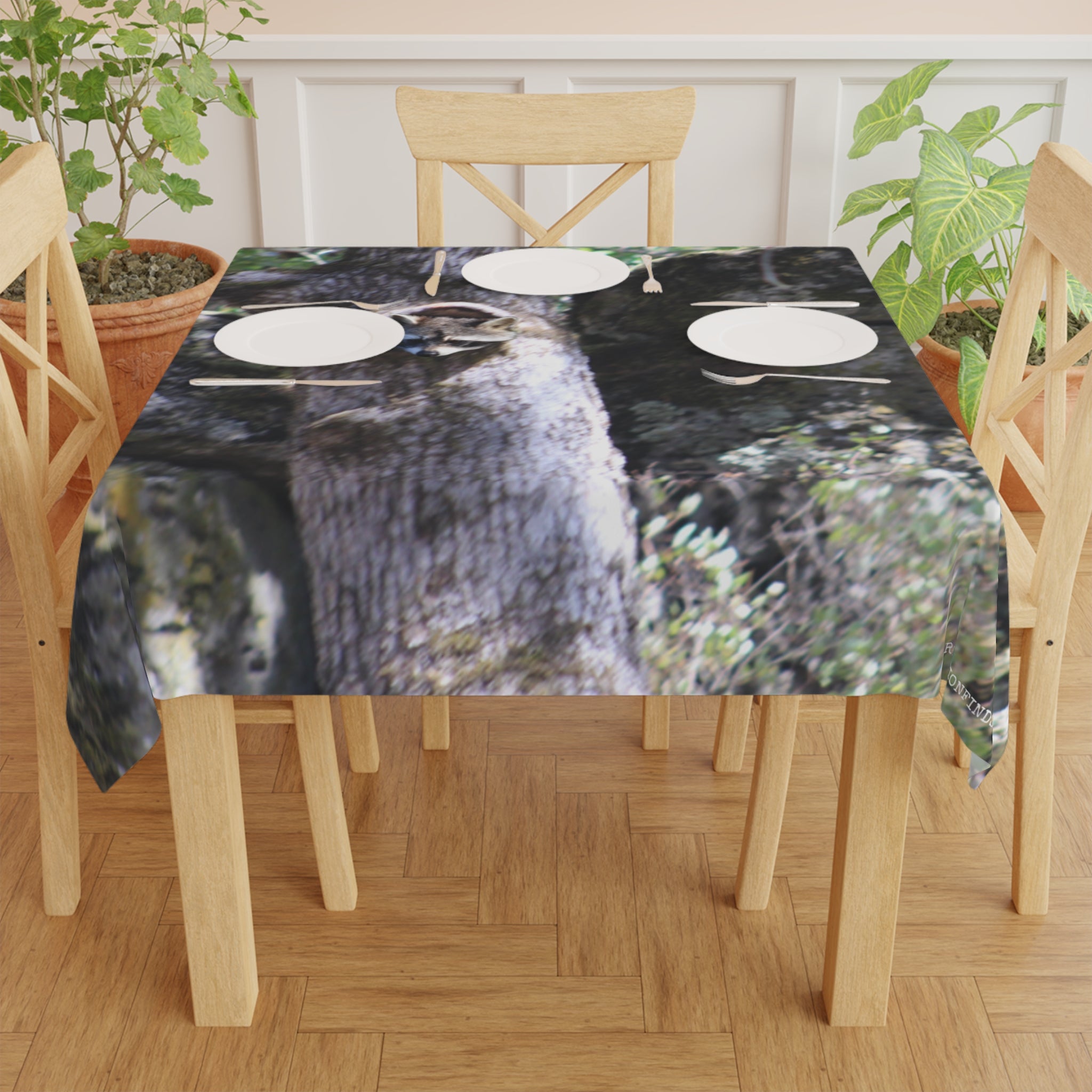 Tablecloth with a raccoon print, set with plates and silverware on a wooden table.