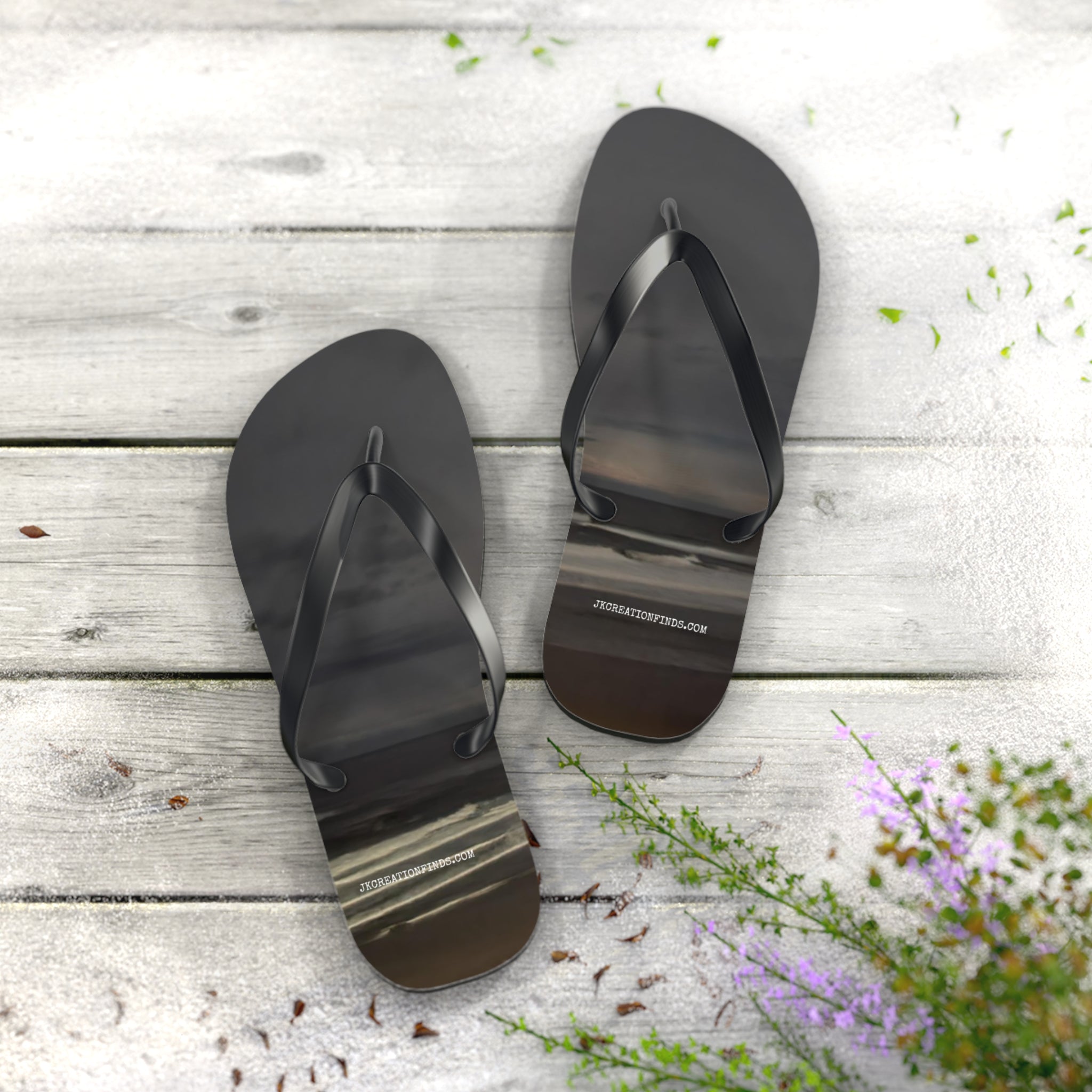 Black flip-flops with a sunset ocean scene printed on the soles, resting on a wooden surface.