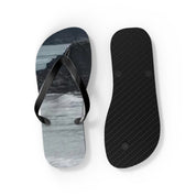 Black flip-flops with patterned soles and ocean background.
