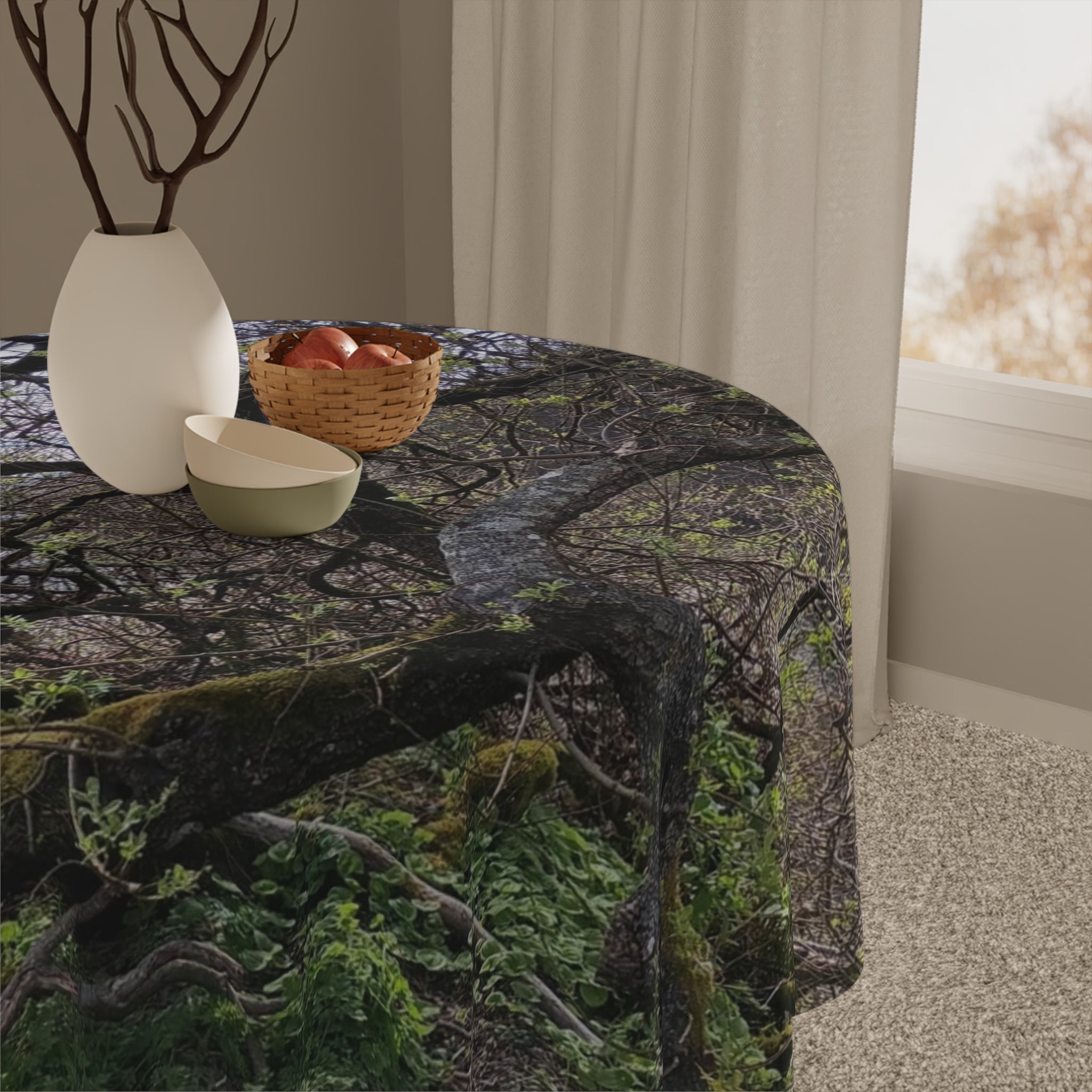 Round tablecloth with forest branch pattern, basket, and vase on a table.