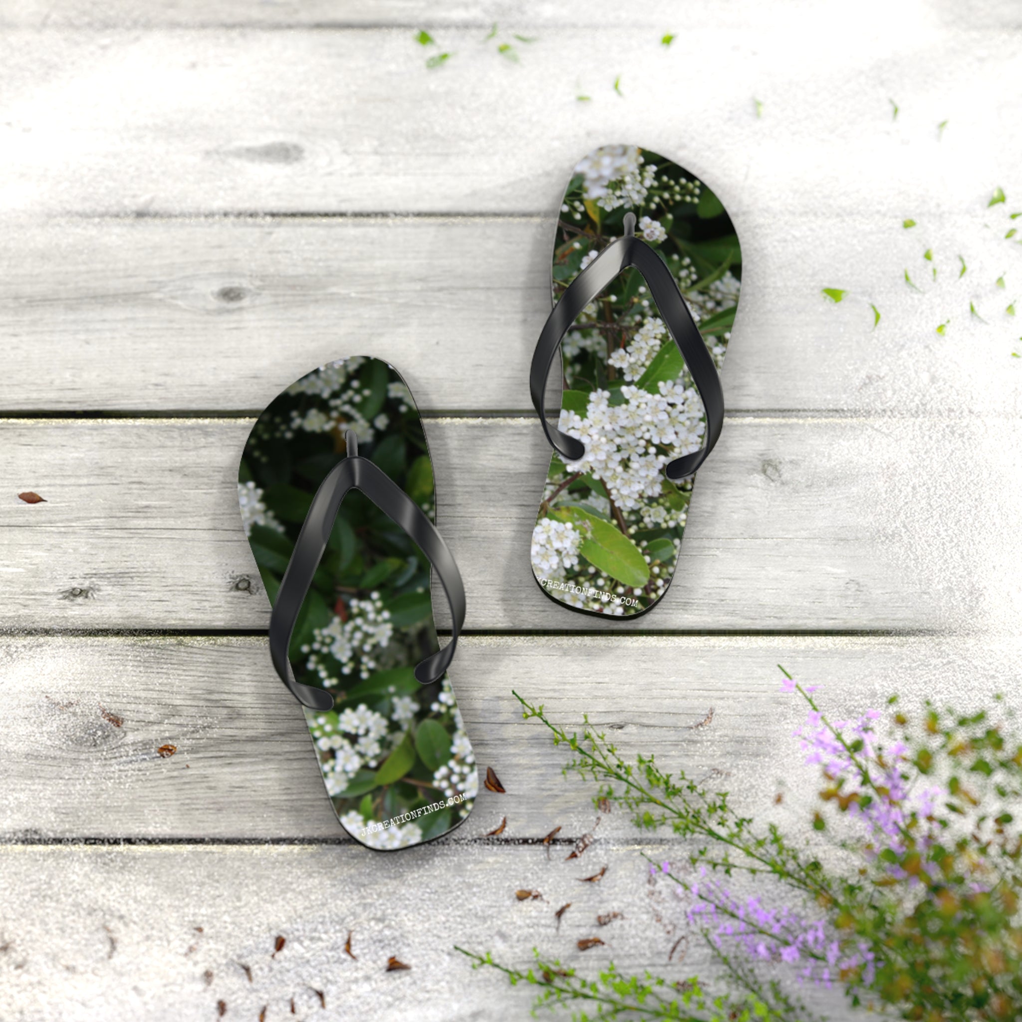 White floral flip-flops on a weathered wooden deck with green foliage.