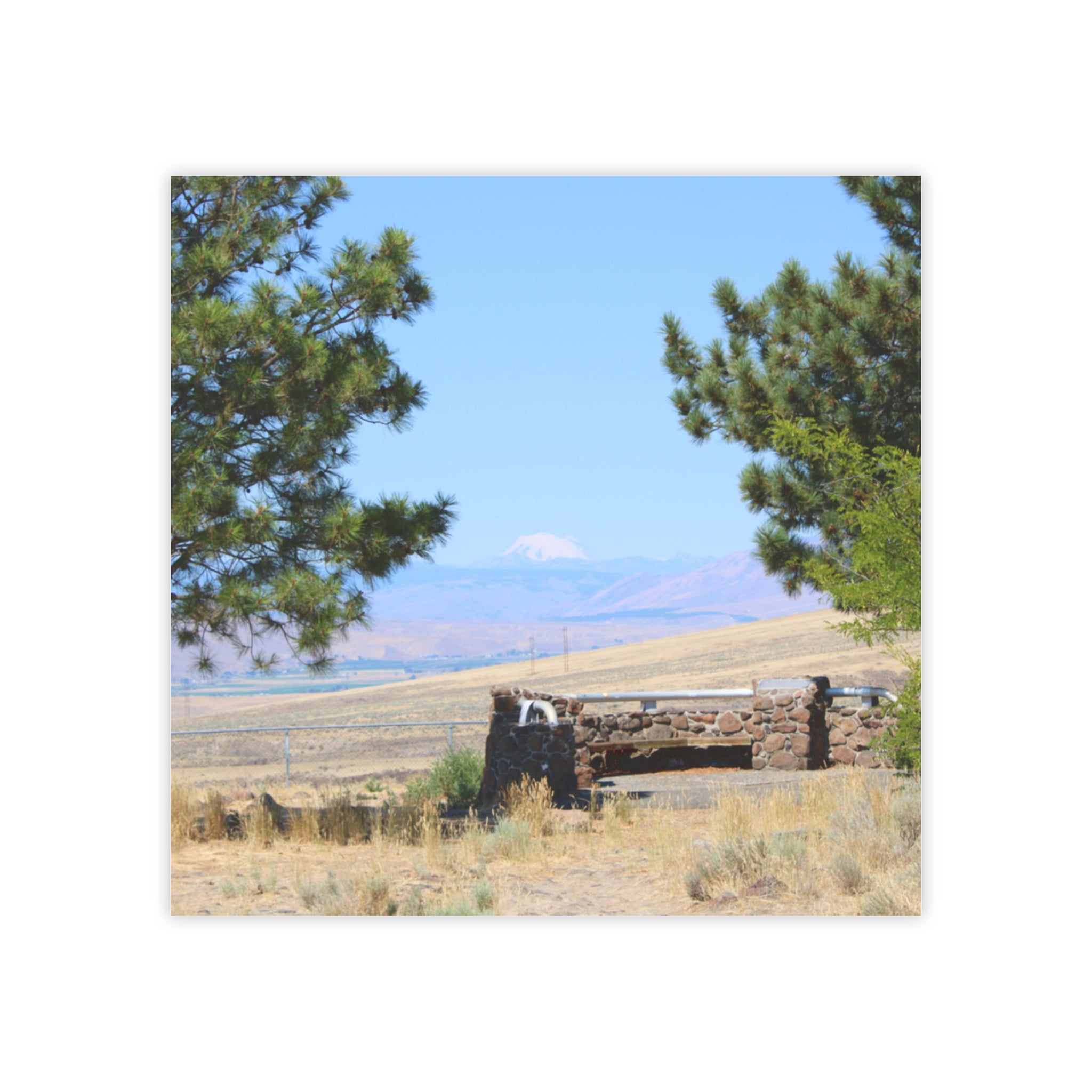 Stone picnic table and fountain framed by pine trees with distant mountain.