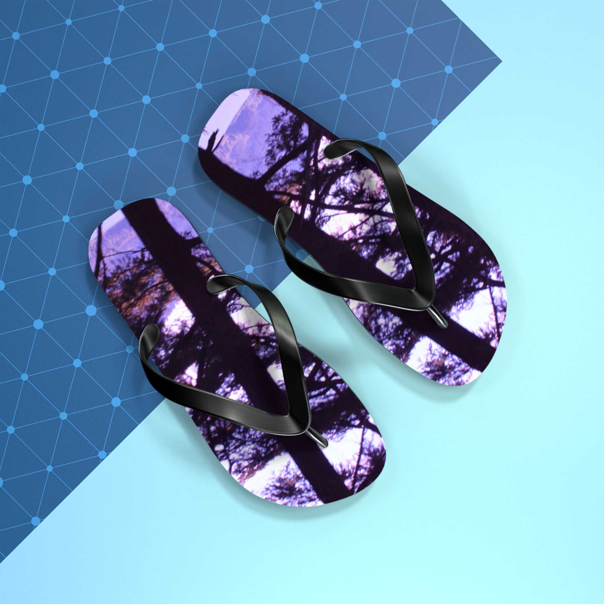Flip-flops with a dark tree silhouette reflection on a blue geometric background.