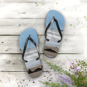 Flip-flops with a beach scene printed on the soles rest on a weathered wood surface.