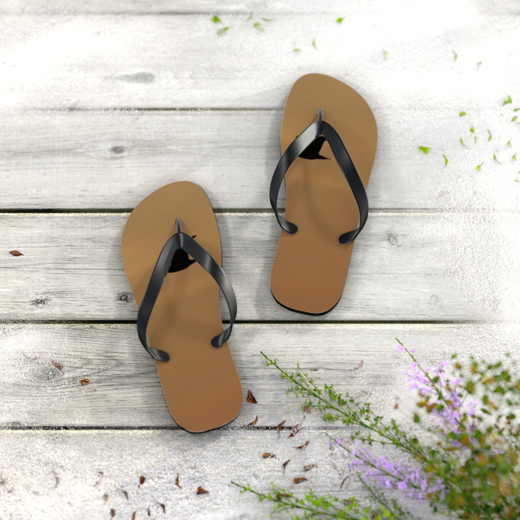 Brown flip-flops with black straps on a light wooden background with green foliage.