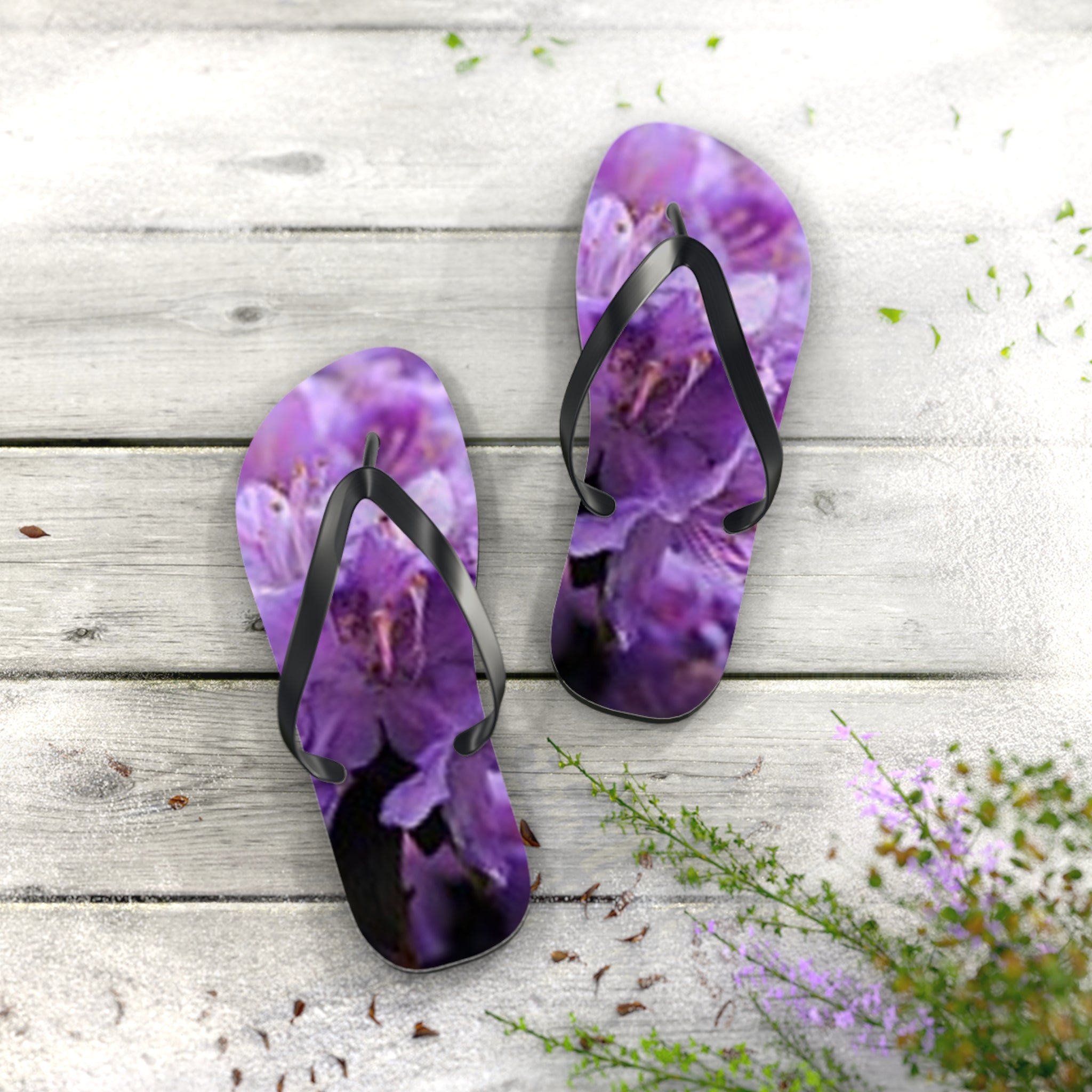 Purple floral flip-flops on a weathered wooden surface with scattered petals.
