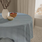 Blue tablecloth draped over a round table with a bowl of apples.