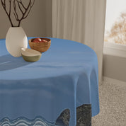 Blue tablecloth draped over a round table with fruit bowl and vase.