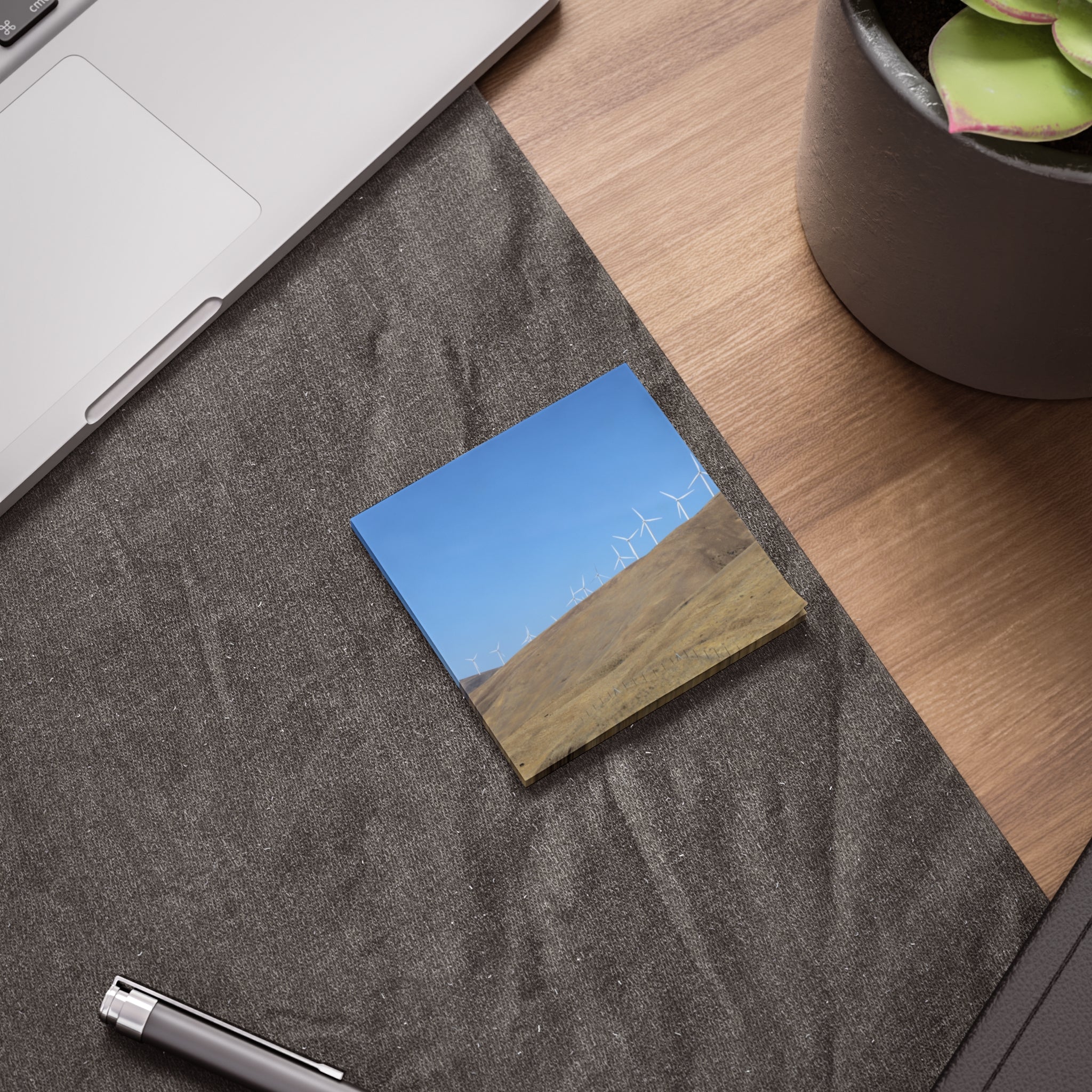 Wind turbines on a grassy hillside under a blue sky, on a sticky note.