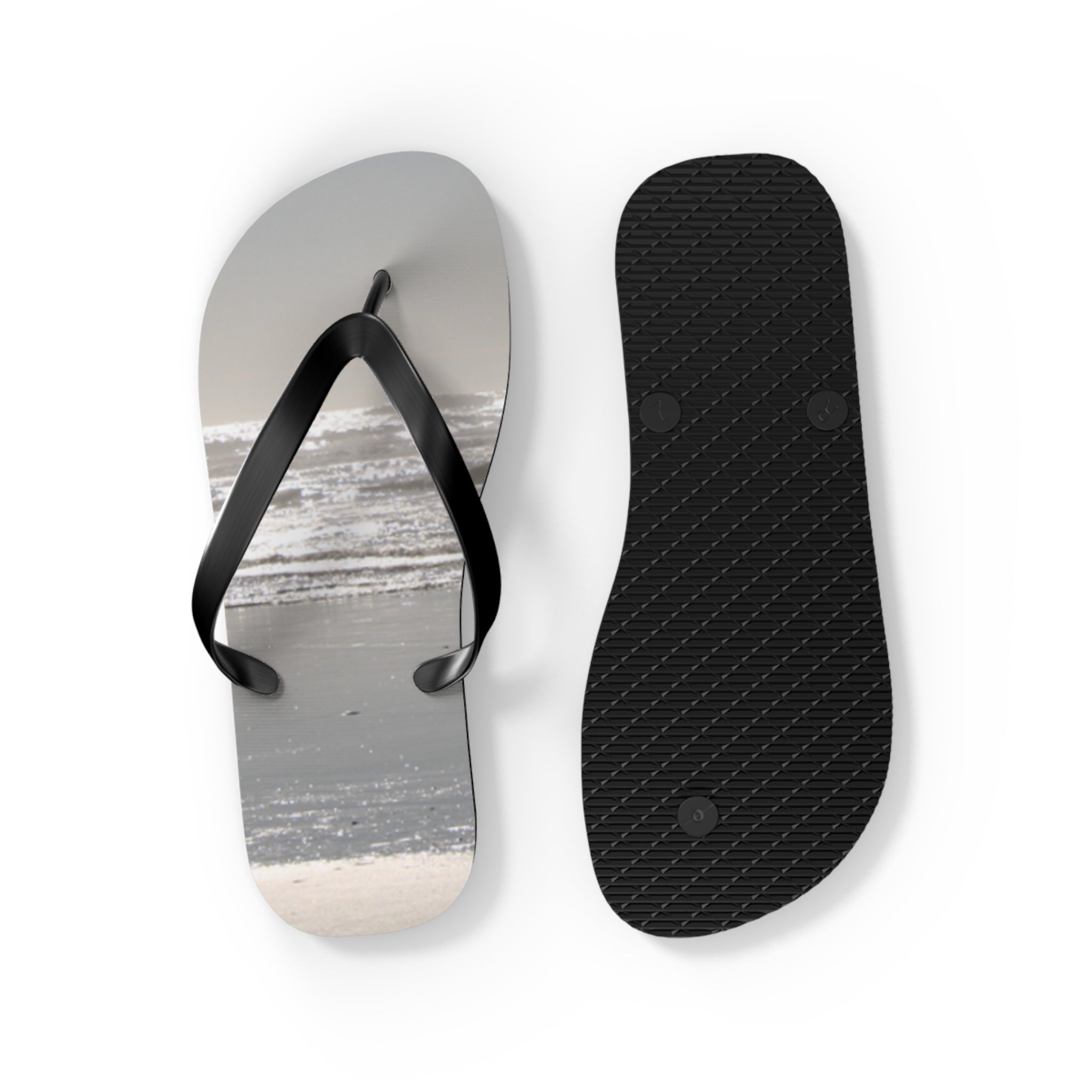 Black flip-flops with white straps, one showing the sole with a beach background.