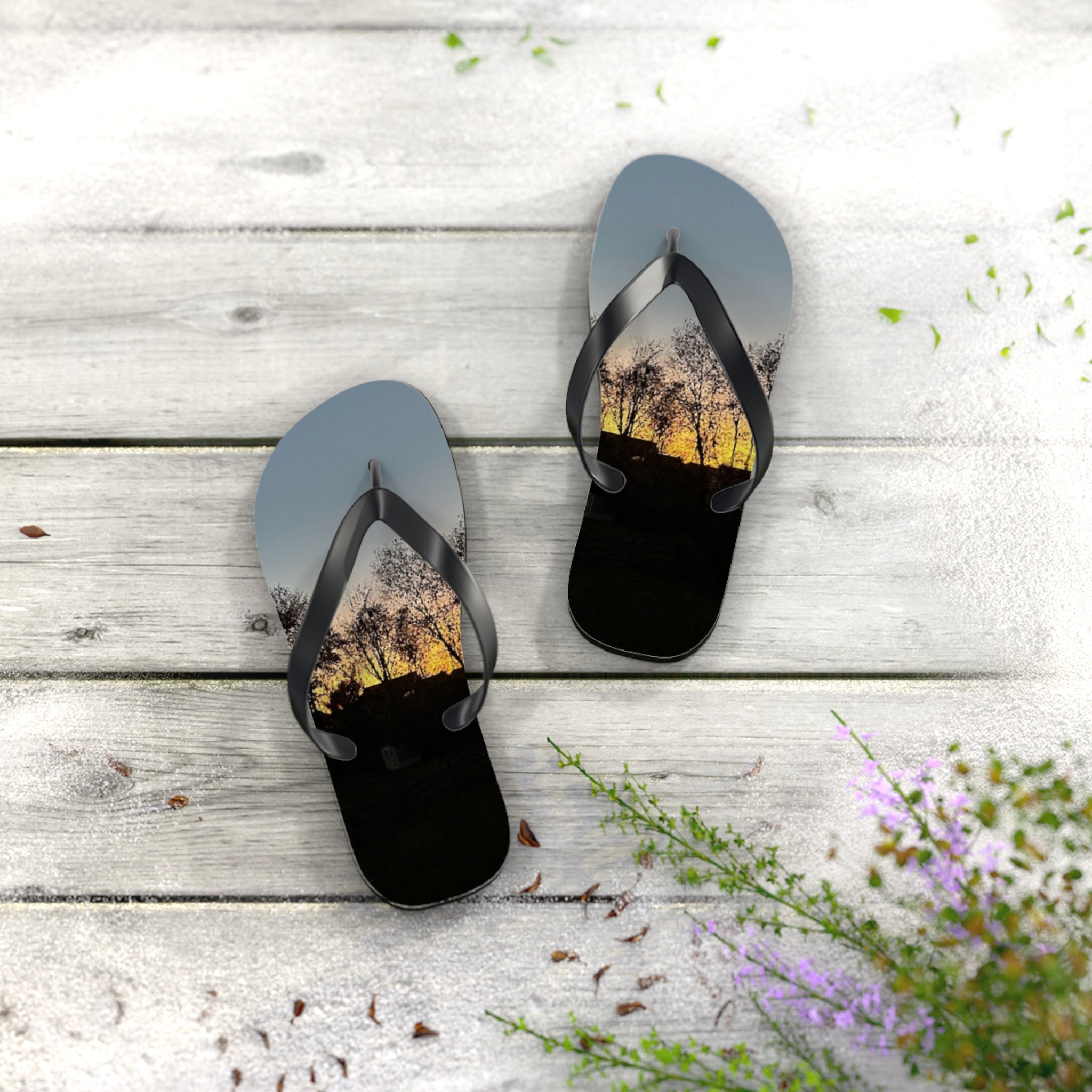 Flip-flops with a sunset tree silhouette on a white wooden surface.