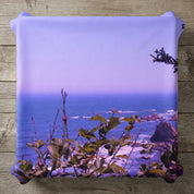 Pillow with a scenic ocean view of waves and rocky coastline.