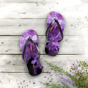 Purple floral flip-flops on weathered wood surface with greenery.