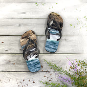 Flip-flops with ocean waves and rocky shore scene on white wooden planks.
