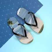 Black flip-flops with a beach scene on the soles, against a blue grid background.