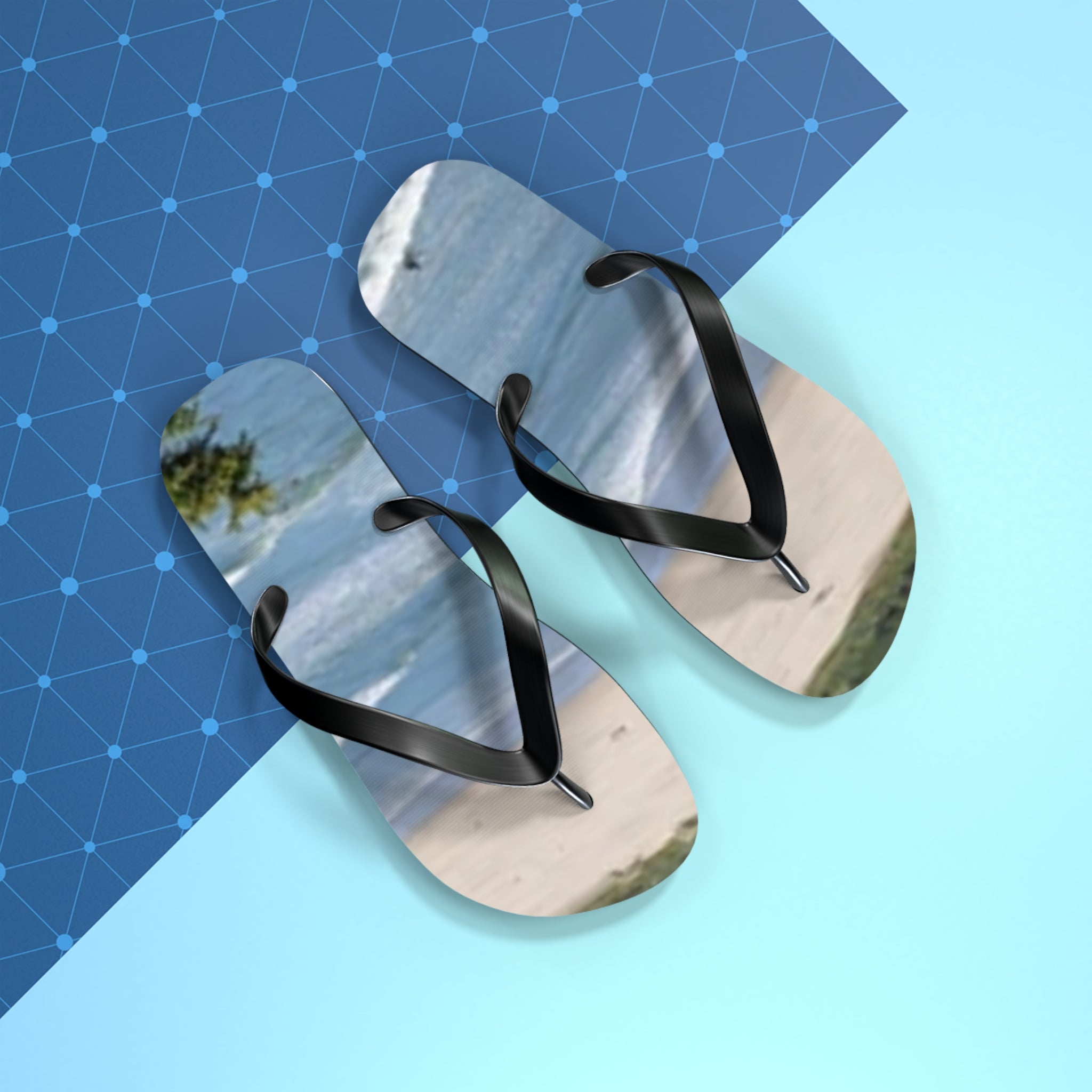 Black flip-flops with a beach scene on the soles, against a blue grid background.