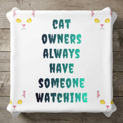 White pillow with cat eyes and text: "CAT OWNERS ALWAYS HAVE SOMEONE WATCHING".
