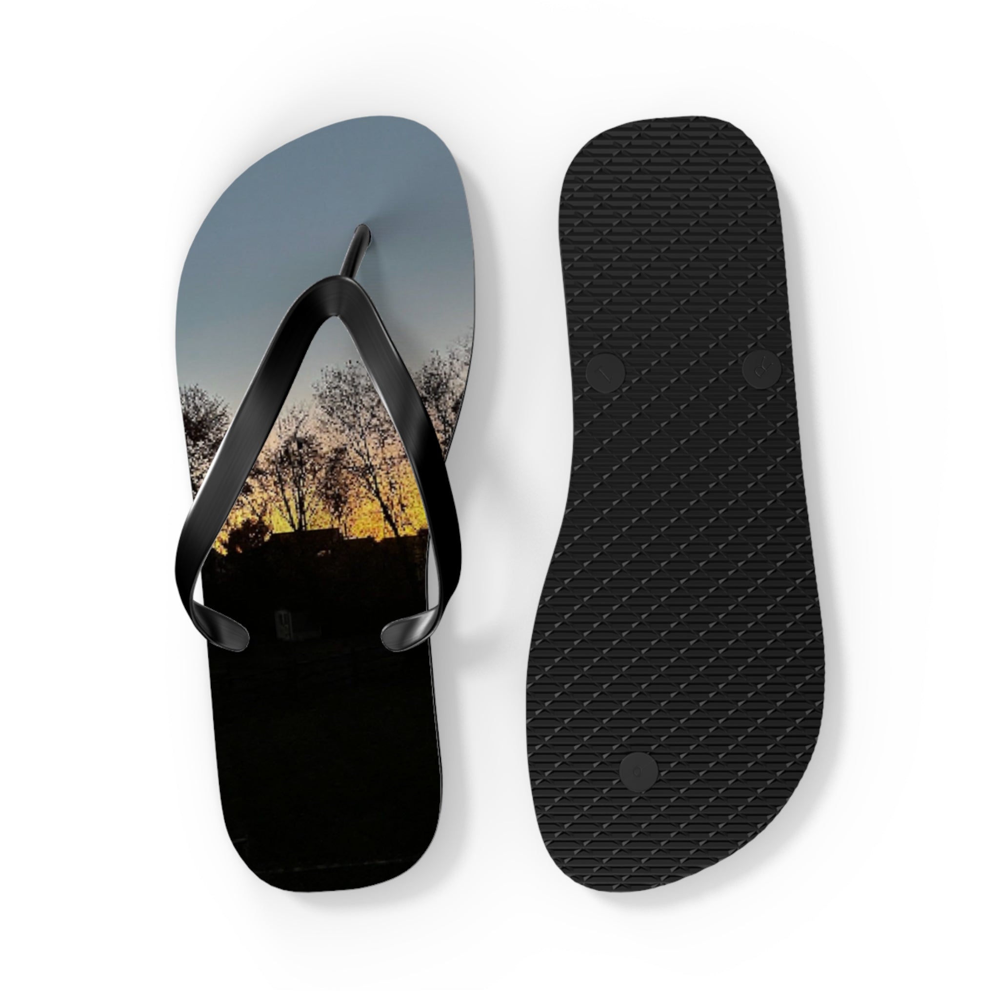 Flip-flops with a sunset landscape image on the left sole and textured black rubber on the right.