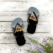 Black flip-flops with sunset trees design on a wooden surface.