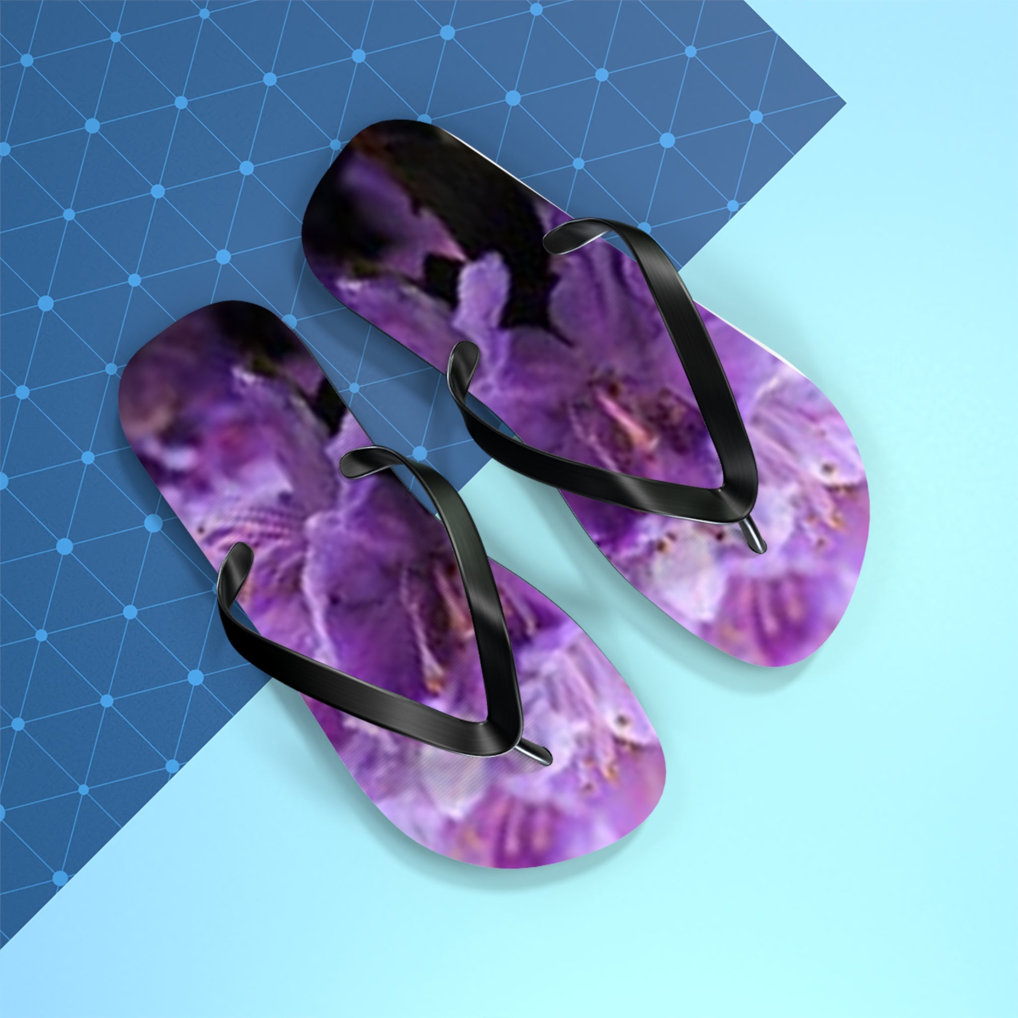 Purple floral flip-flops with black straps on a blue and light blue background.