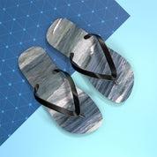 Black flip-flops with a crashing wave design on a blue and grey background.
