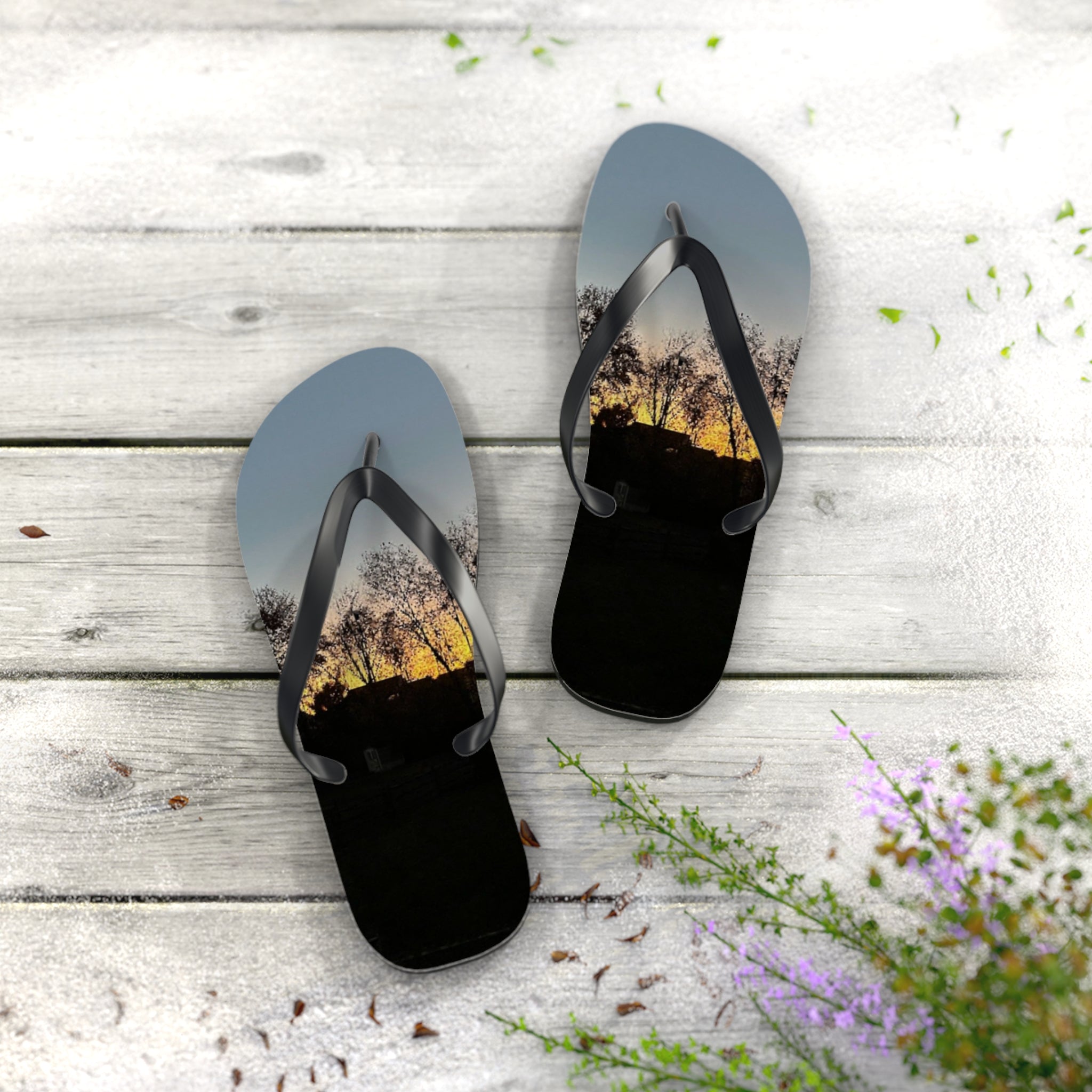 Flip-flops with a sunset tree silhouette on a wooden background.
