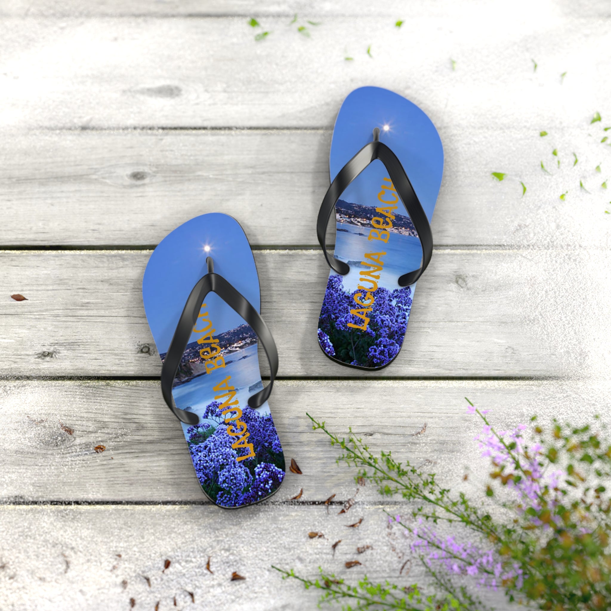 Blue flip-flops with "Laguna Beach" text and purple flowers on a wooden surface.