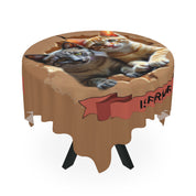 Two tabby cats peek out of a torn cardboard box on a round tablecloth.