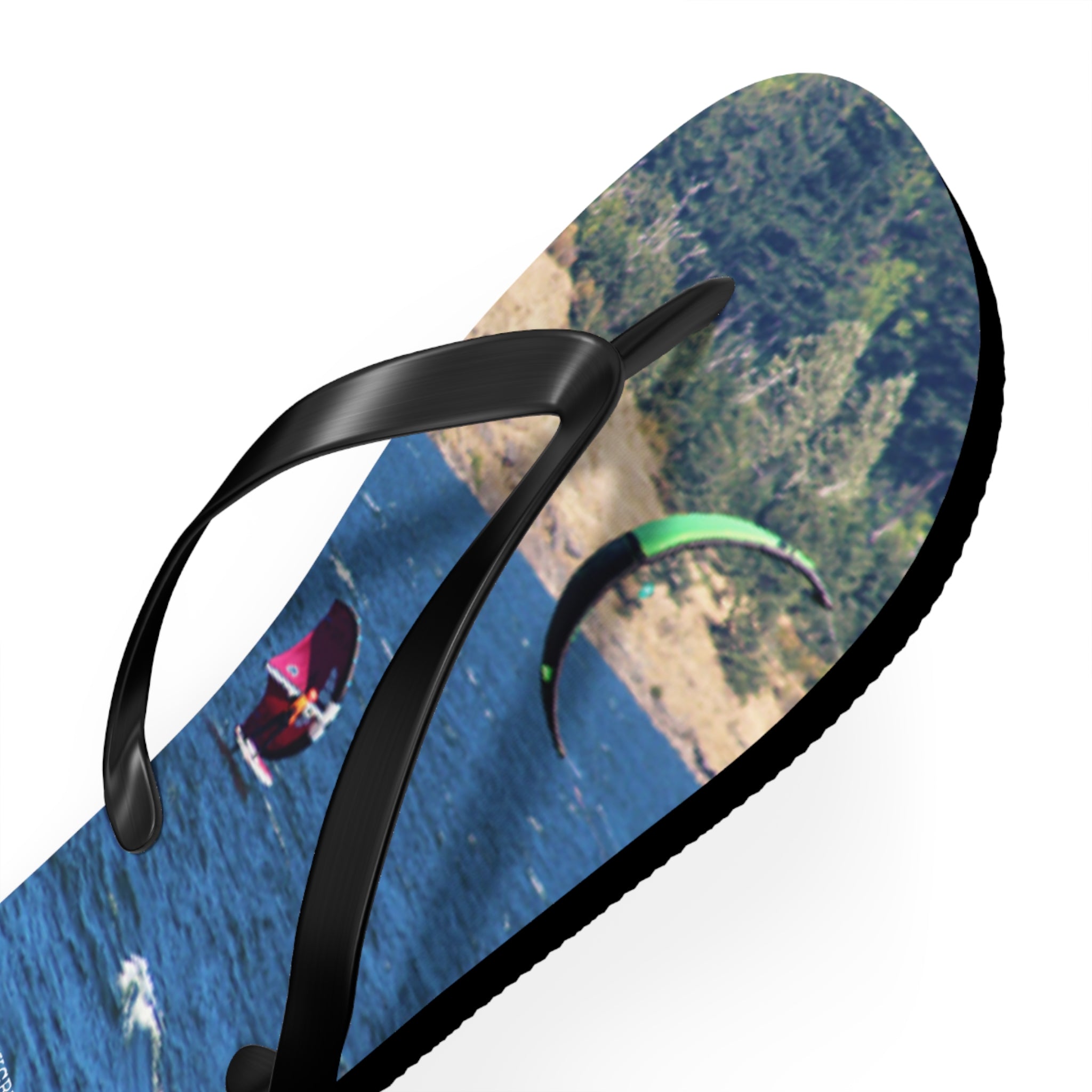 Flip-flop with kitesurfers on ocean waves and forested shoreline.
