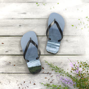 Flip-flops with ocean waves and green hills on a weathered wooden surface.